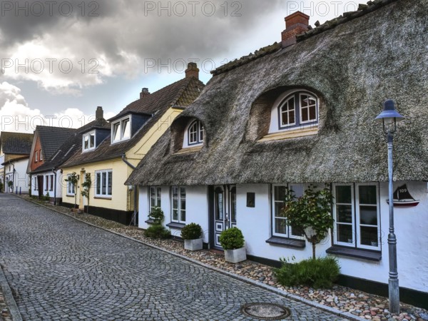 Traditional houses with thatched roofs and cobblestone streets under a cloudy sky, maasholm, germany