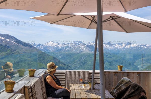 Woman Sitting in a Restaurant Terrace with Mountain View with Snow and Sky in a Sunny Summer Day in Andermatt, Uri, Switzerland