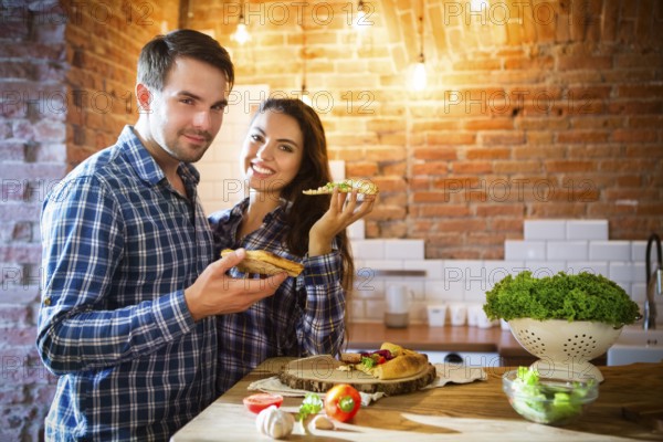 Young smiling couple eating homemade pizza together at kitchen