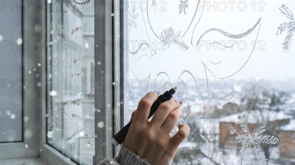 Female hand painting Christmas deer painted on window glass. Christmas winter decor on the window glass. White pattern of deer. Snow art tracery window on holiday season. Diy. Hygge home