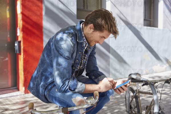 Young man using smartphone in a bicycle with jeans denim outdoor