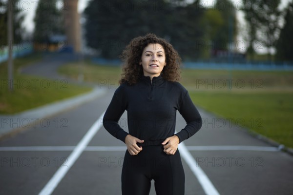 Woman standing on a road in sportswear, surrounded by greenery