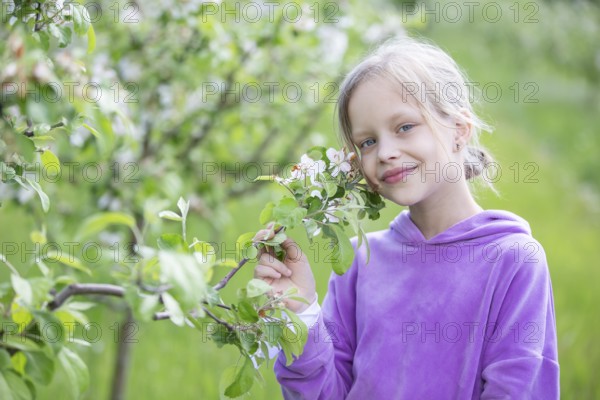 May 27, 2021. Belarus, Gomel, Public event.A beautiful little blonde woman poses in a spring garden against the backdrop of a blooming apple tree. A child with blue eyes and blond hair