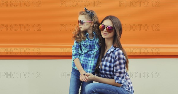 Beautiful stylish mother and child daughter together, happy mom with kid girl in glasses, casual clothing in the city