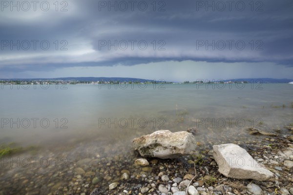 Stormy sky over a calm lakeshore with stones and clear water, Allensbach, Untersee, Lake Constance, Constance District, Baden-Württemberg, Germany