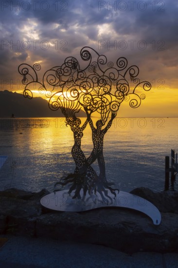 Montreux, Switzerland, October 12, 2019: Metal figure of a woman and man at promenade of Geneva Lake, colorful blue and yellow sunset