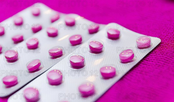 Pink pills in a blister on a pink background close up