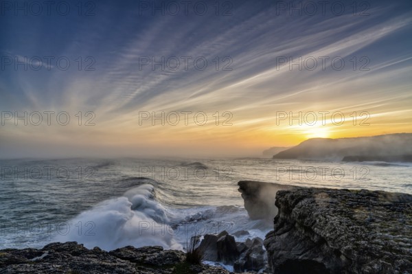 A view of huge storm surge ocean waves crashing onto shore and cliffs at sunrise