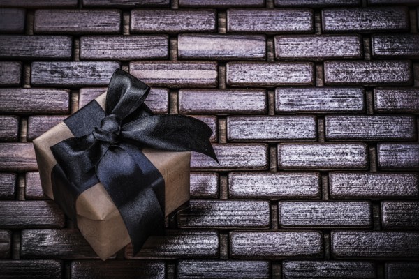Wrapped present box with black ribbon on wicker wooden mat