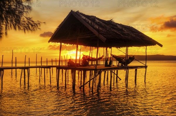 Native people relaxing in hammocks on wooden jetty during sunset on Kri island, Raja Ampat, West Papua, Indonesia