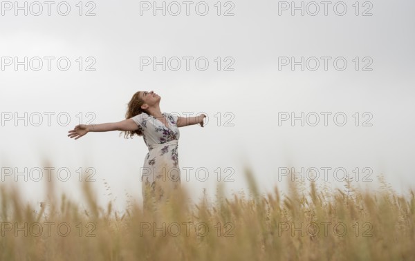 Happy woman in a floral dress stands amidst golden wheat, enjoying the serene landscape