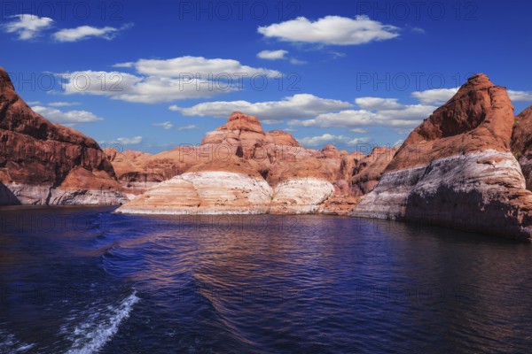 The foamy trace from powerboat crosses emerald waters. Hills from red sandstone surround the lake. The lake Powell on river Colorado