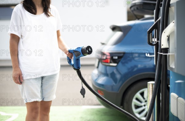 Woman charge her Electric car on gas station. Blue car and electric plug for charging. Ecology fuell concept