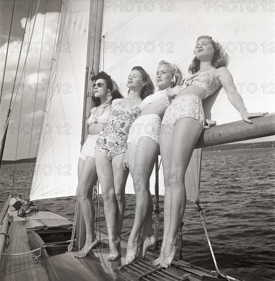 1940s sailing boat. Four young women are standing and leaning against the sails of the boat and enjoys the sunshine and wind. They are wearing the typical 1940s bathingsuit and bikini with high waist. Sweden 1946 Photo Kristoffersson ref AC101-3