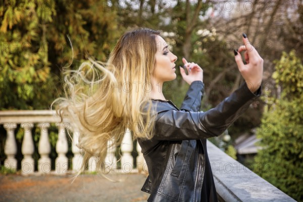 Side view of young woman standing near parapet with her hair flying in the air and outstretched arms