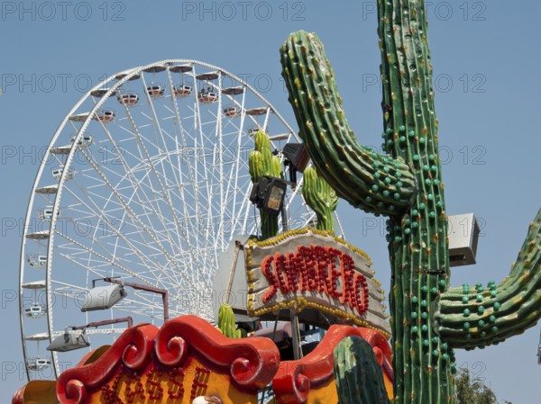 Colourful amusement park with a large Ferris wheel and decorative cacti under a clear sky, Vienna, Austria