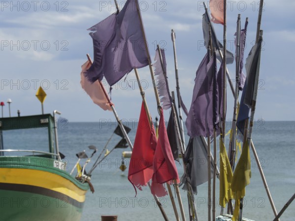 Colourful flags waving in the wind, next to a green boat in front of a wide sea and blue sky, sopot, baltic sea, poland