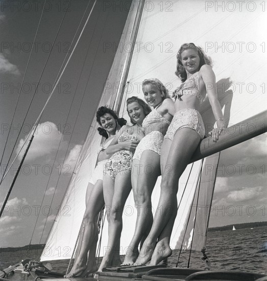 1940s sailing boat. Four young women are standing and leaning against the sails of the boat and enjoys the sunshine and wind. They are wearing the typical 1940s bathingsuit and bikini with high waist. Sweden 1946 Photo Kristoffersson ref AC100-3