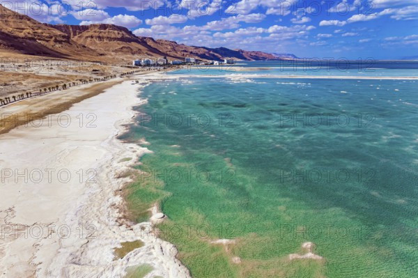 Magnificent Dead Sea. Drone footage. Bright March day. The water reflects the bright blue of the sky. Lush cumulus clouds are reflected in the water. Evaporated salt protrudes from the water