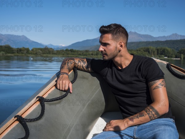 Portrait of young handsome man with tattooed body looking at camera sailing in boat