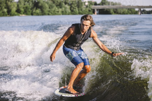 Young athletic man with long hair wakesurfing on waves of river in sunny summer weather. Ttheme outdoor activities in summer. Water sports wakesurf on the board. sliding wakeboarder in water splash