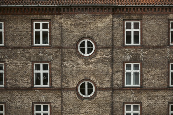 Symmetrical brick building façade with square and round windows, displaying traditional architectural style in Copenhagen, Denmark