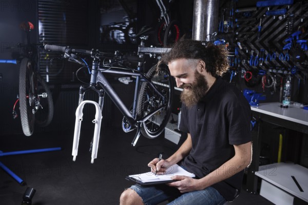 Bicycle Workshop Technician Doing Administrative Work. Bicycle mechanic writing in his checklist notebook. Bicycle mechanic at work. Caucasian worker writing on clipboard in bicycle shop