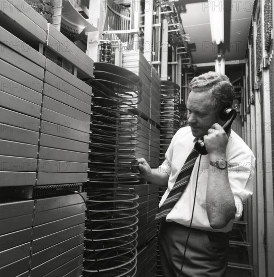 Telephony in the 1970s. A man in a room with an automatic switchboard connecting the calls through a mechanical device that connected the calling and receiving parts. The manufacturer is LM Ericsson. Sweden 1971 Kristoffersson ref ED