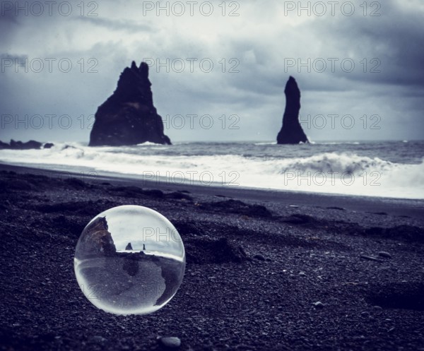 Cold sea water rolling on wet sand near rough stony cliffs on stormy day on Reynisfjara Black Beach in Iceland