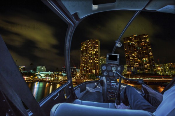 Helicopter cockpit flies in Honolulu skyline by night, Oahu, Hawaii, with pilot arm and control board inside the cabin