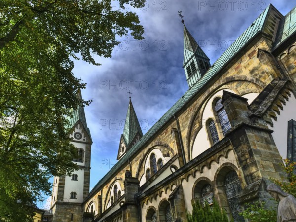 An imposing church with several towers against a blue sky, surrounded by trees, Werl, North Rhine-Westphalia, Germany