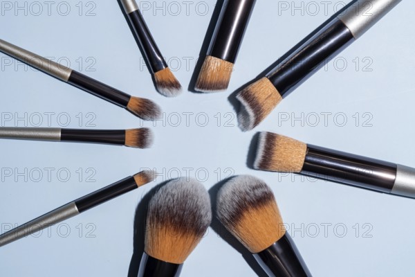 Make up brush sets arranged in a circle on blue background, top view with copy space. Cosmetics products
