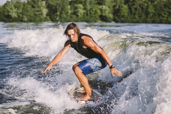 Young athletic man with long hair wakesurfing on waves of river in sunny summer weather. Ttheme outdoor activities in summer. Water sports wakesurf on the board. sliding wakeboarder in water splash