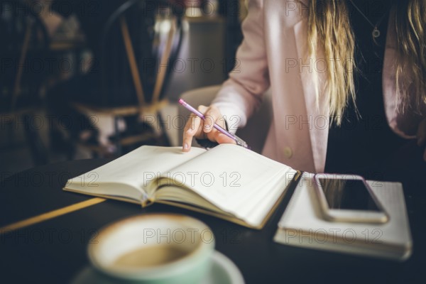 Business, education concept. Woman working in outdoor at coffee shop. Close up caucasian woman hand on wooden table inside cafe makes notes in notebook. Writing dairy on notebook