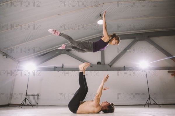 Young couple Couple practicing acro yoga in gym. Healthy lifestyle. Acroyoga. Couple yoga. Partner yoga. Muscular man throwing women to air. Concept of trust, strength and courage