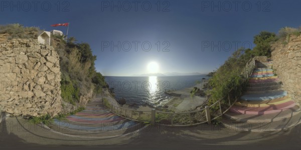 360 photo - Colourful stairs leading down the rocky coast from the hotel area. Waterside scene with bright sun shining and sparkling on sea surface, mountains on the horizon. Antalya scene, Turkey