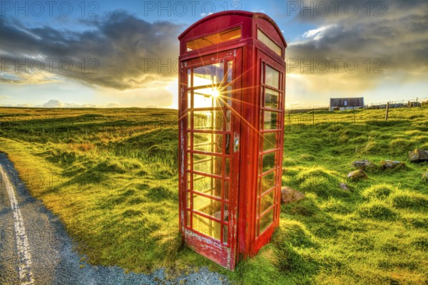 Urban red telephone box in the middle of a green countryside. Concept for synergy between modern and rural area. Red and green complementary colors join together in a scottish land, United Kingdom