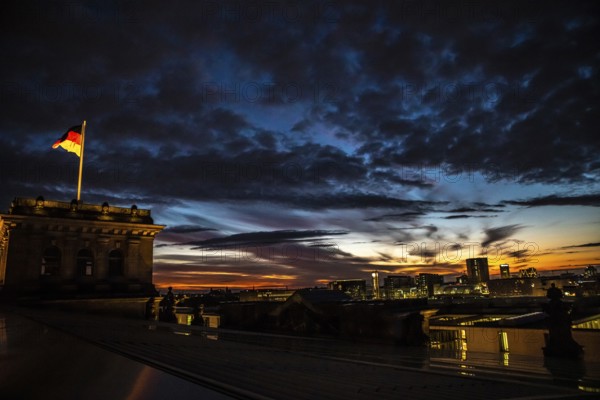 The Berlin Reichstag with evening sky with the flag of Germany and clouds in the background. The Berlin Reichstag with evening sky with the flag of Germany