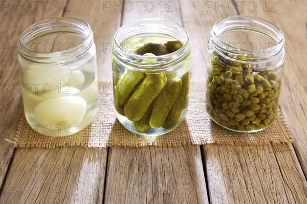 Bottled pickles as capers onion and cucumbers in wooden table
