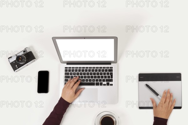 Clean and modern workplace. Notebook, coffee, graphic tablet, phone, camera and to do list and female hands from above