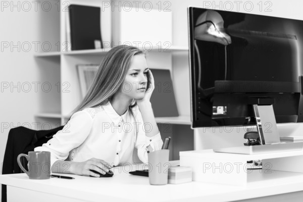 Young pretty business woman sitting at the desk with computer in blue office