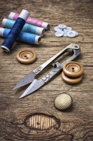 Scissors, thread and buttons on unhewn darianna background in vintage style