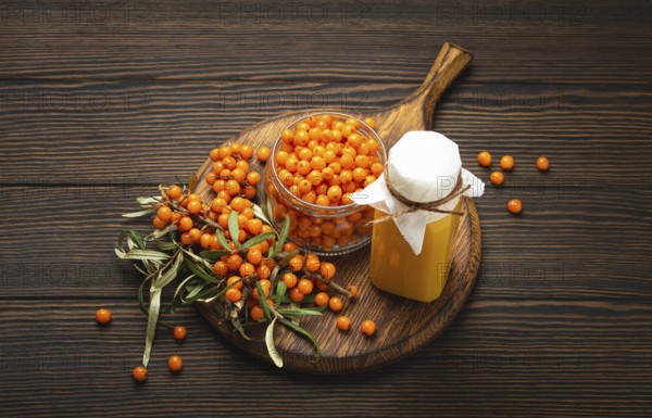 Sea buckthorn healthy drink in bottle, ripe berries in glass jar and branches with leaves top view on dark wooden rustic background, great for skin, heart, vessels and immune system, food photography, food photography