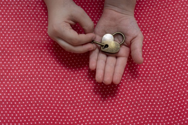 Hand holding a heart shaped lock and key on a red background