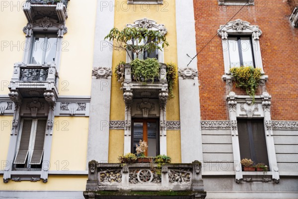 Facade of the building with stucco, balconies and flowerpots. Milan, Italy.