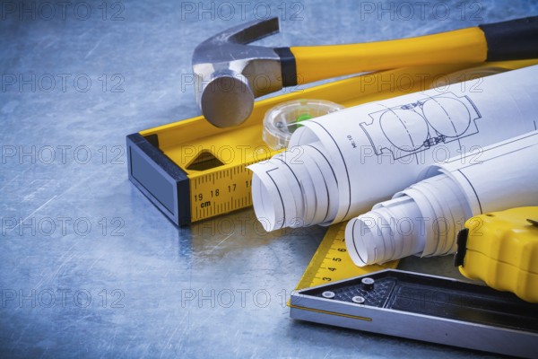 Close up image of hammer measuring line construction plans and level square ruler on metallic background maintenance concept