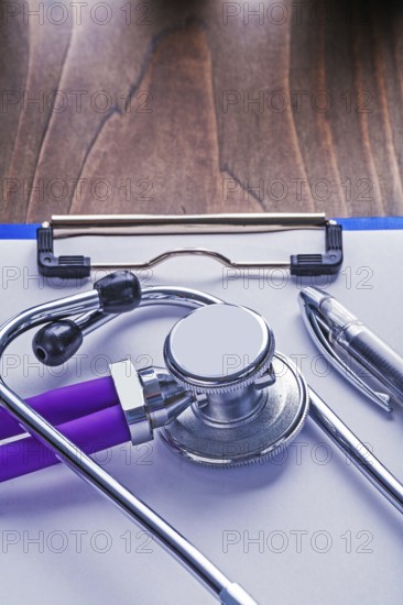 Stethoscope with purple tubes and ballpoint pen on paper in clipboard and vintage wooden board vertical version