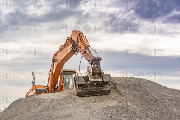 Frontal view of an orange excavator climbed on top of a ballast pile