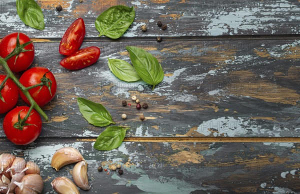 Food cooking border with cherry tomatoes, fresh green basil and garlic cloves top view on rustic colourful wooden background, ingredients for preparing meal, copy space, food photography, food photography