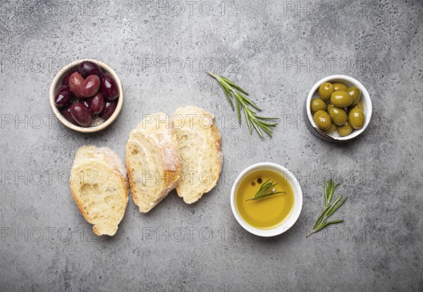 Slices of fresh ciabatta, green and brown olives, olive oil with rosemary, olive tree branches on gray concrete stone rustic background overhead, food photography, food photography
